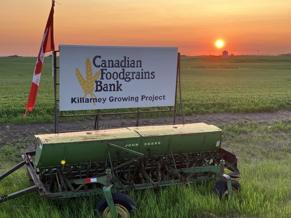 an old John Deere seeder on the side of a field with a sign that ready 'Canadian Foodgrains Bank'