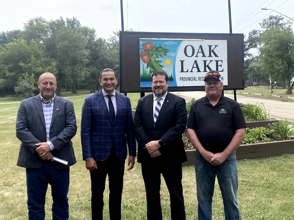 four men standing together in front of a sign that reads 'Oak Lake'