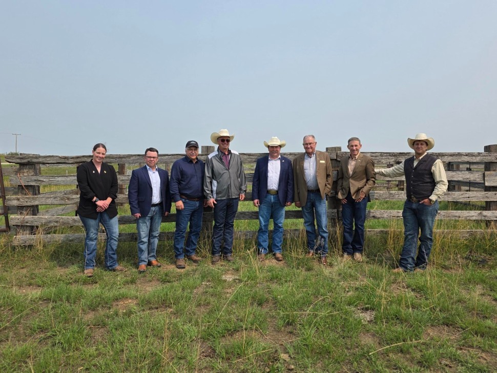 Saskatchewan Agriculture Minister Daryl Harrison with producer group representatives standing in front of a wooden fence
