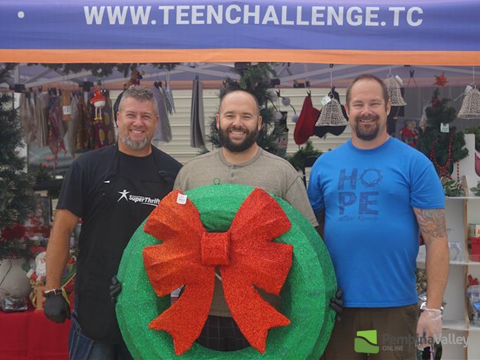 three men stand with a large wreath
