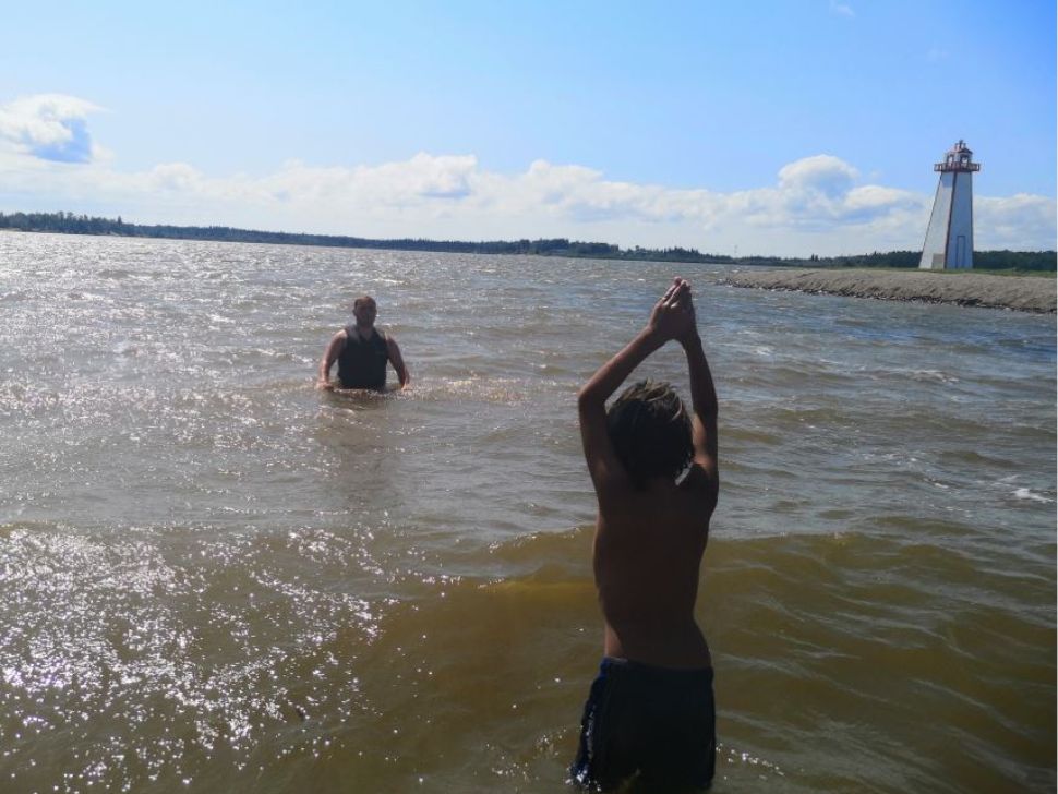 A boy and his father enjoy the beach at a lake in Manitoba, with a lighthouse in the distance. 