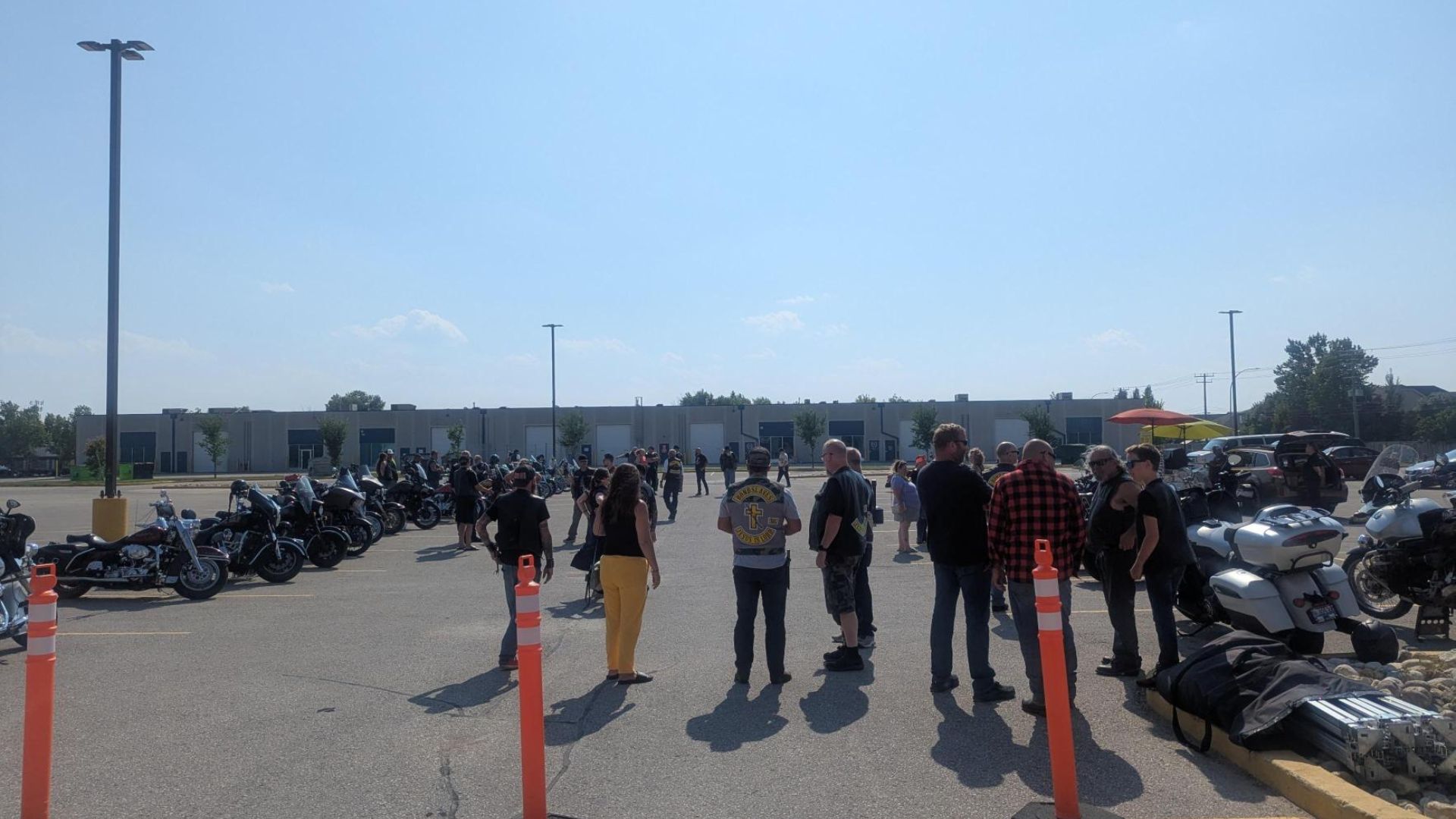 A large group of bikers in a parking lot with their bikes lined up at the sides.