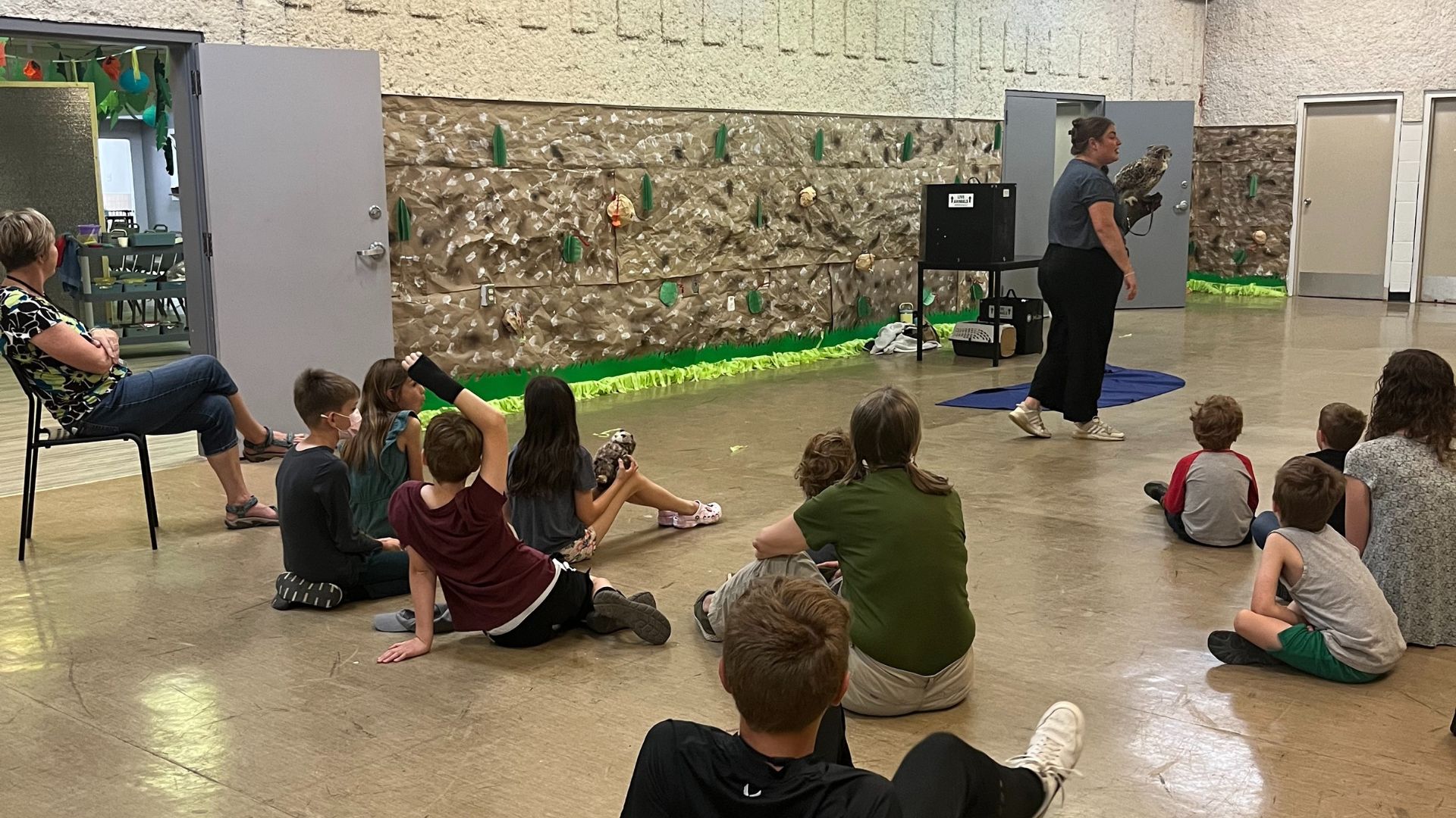A group of summer campers watching a woman give a wildlife presentation with an owl on her hand.