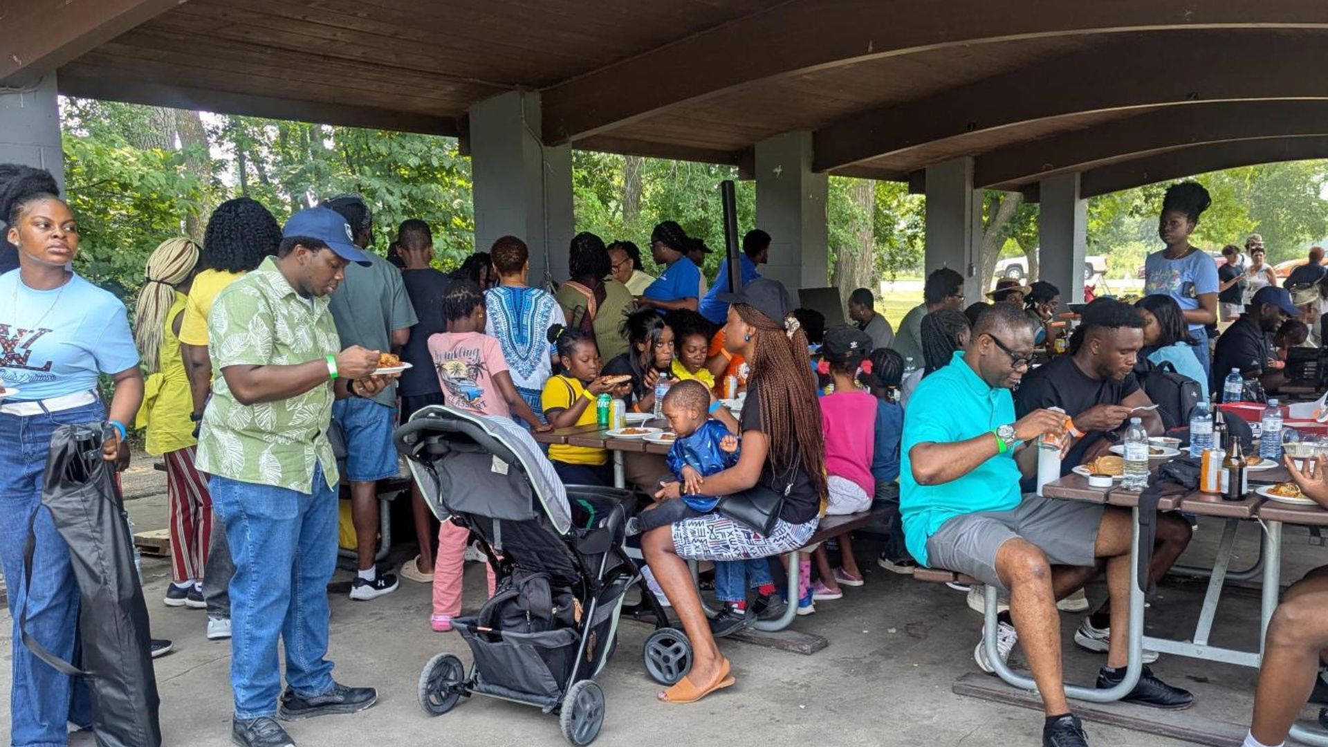 A group of 30 to 40 people eating underneath a park shelter.