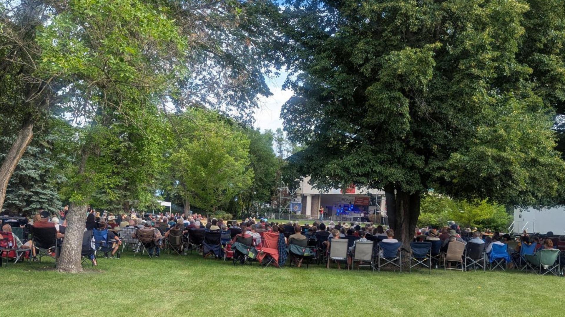 200 people sitting in a park surrounded by trees for a Sunday morning community worship service