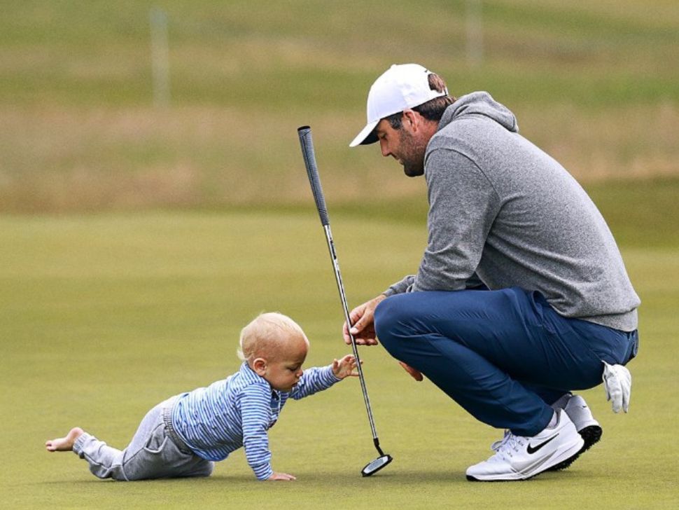 Scottie Scheffler on a golf green with his young son, holding a golf club.