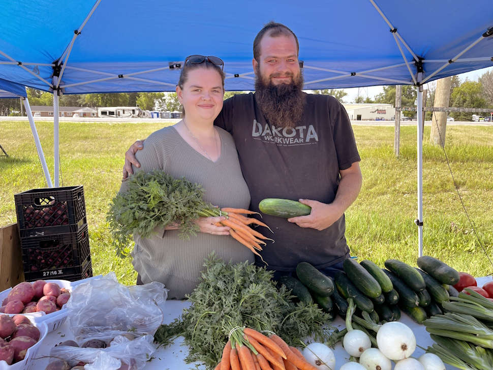 Kyle and Rebecca Gingrich standing behind a table full of fresh vegetables at the West End Tim Hortons parking lot market.