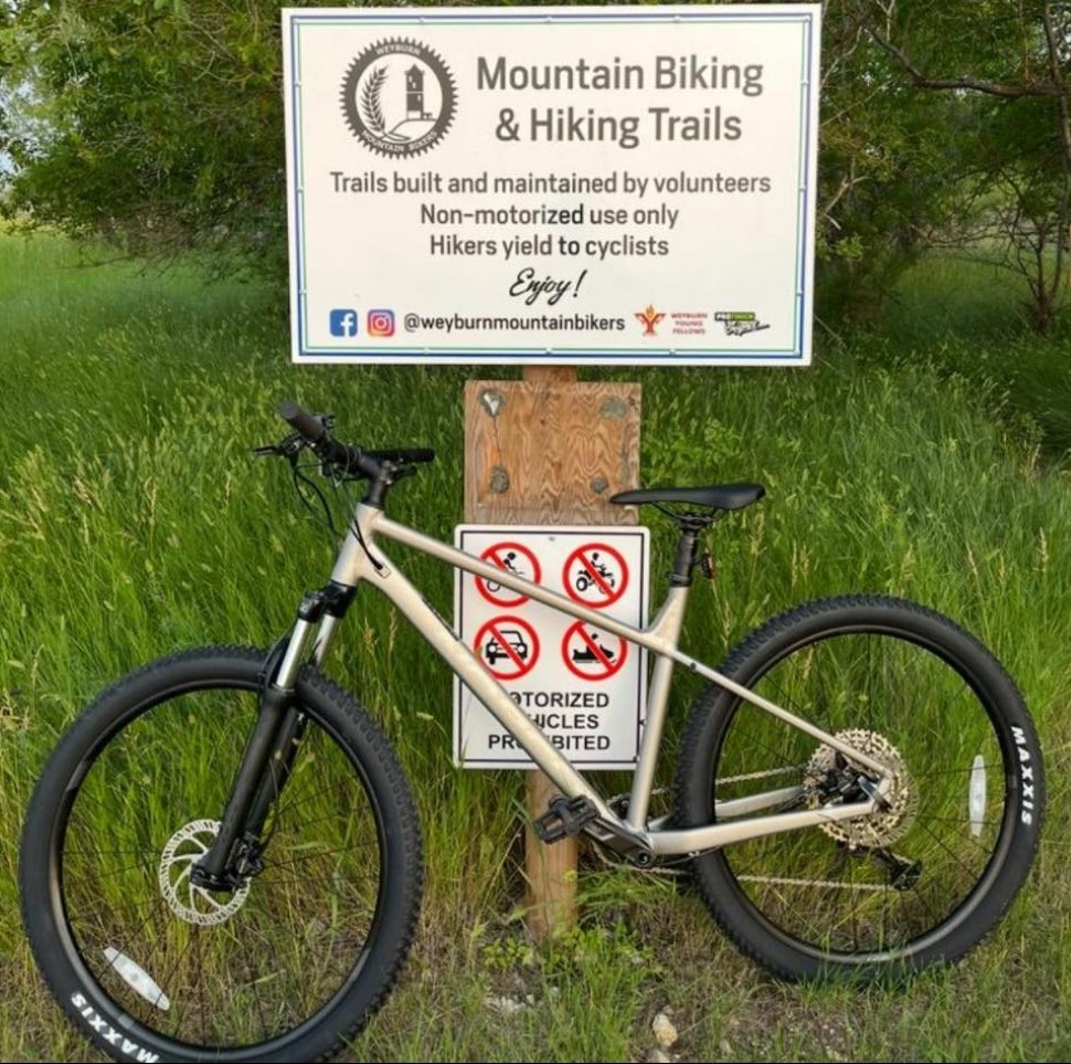 A mountain bike resting against a sign post with a sign indicating it is a mountain bike trail