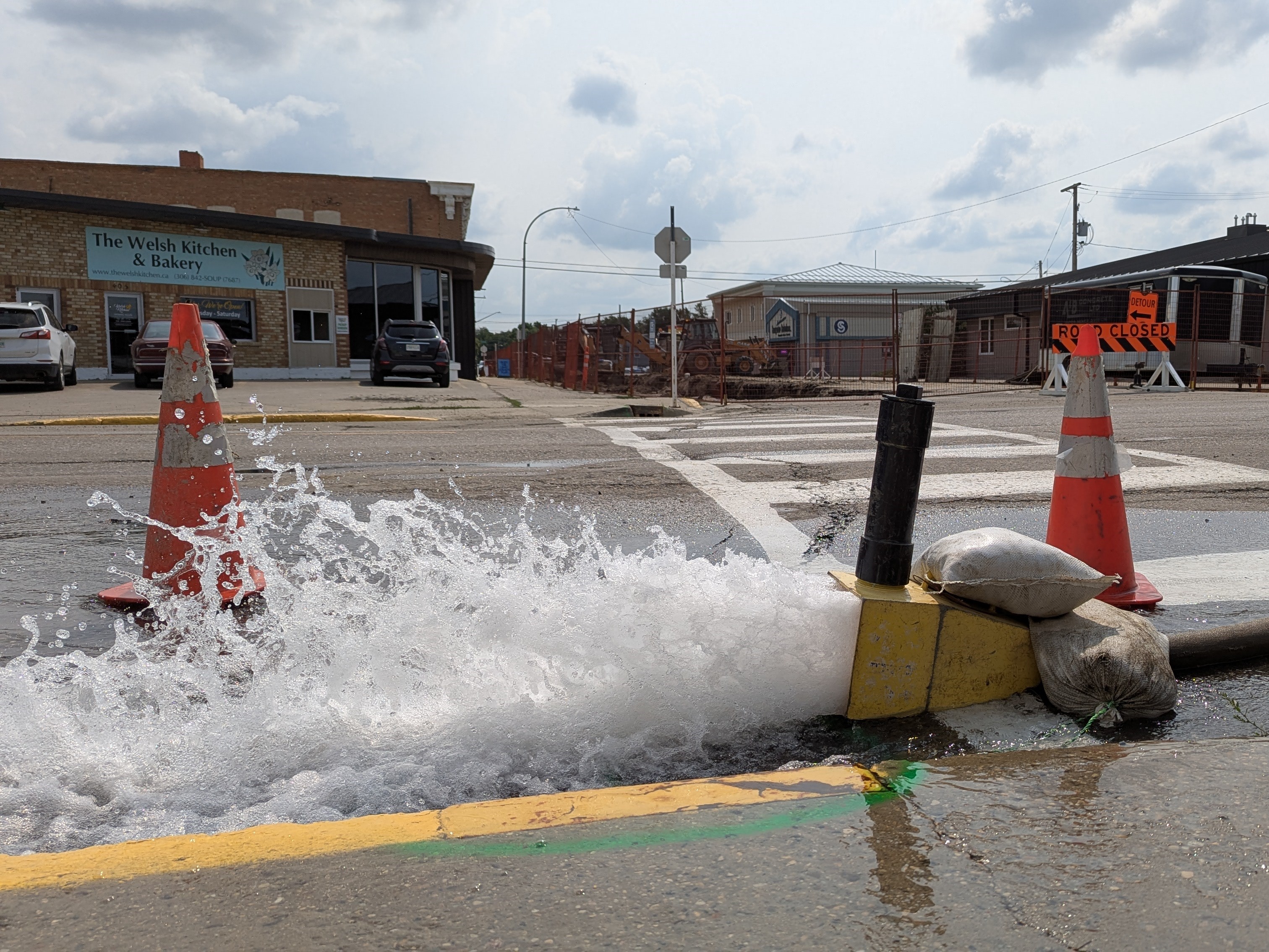 A hose with water gushing forth with construction taking place in the background