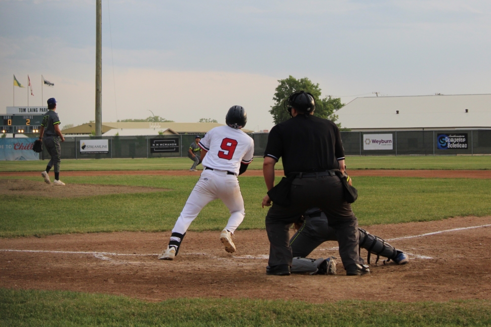 A baseball player in a white uniform watch a batted ball fly