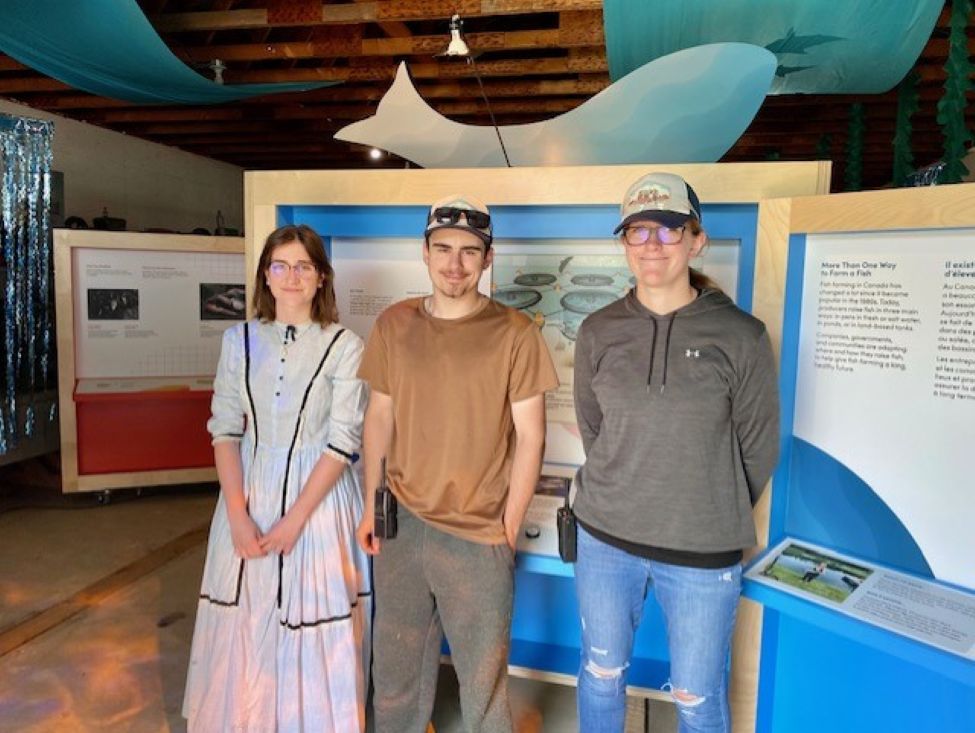 three young adults, two young women and a young man, pose for a picture at a museum display