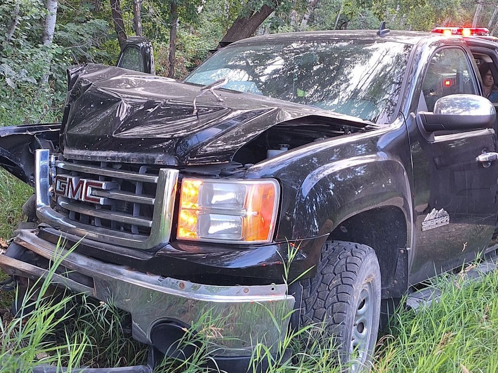 Damaged pickup truck in a ditch with a crumpled front end after hitting a tree.