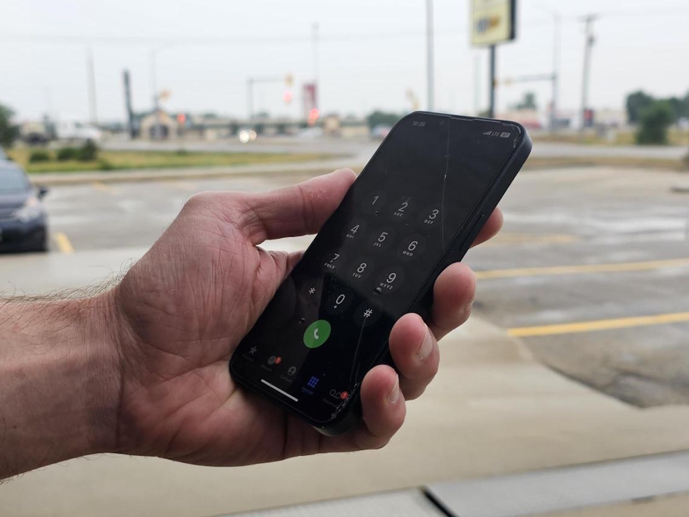 A close-up of a hand holding a smartphone with low signal bars on the screen.