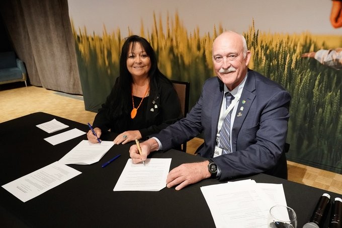  Kallie Wood, President and CEO of NCIAF seated at a table with Keith Currie, President of the Canadian Federation of Agriculture  to sign MOU