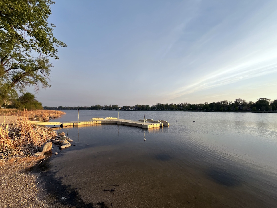 Crescent Lake in Portage la Prairie with low water levels, surrounded by greenery and visible shoreline, under a summer sky.