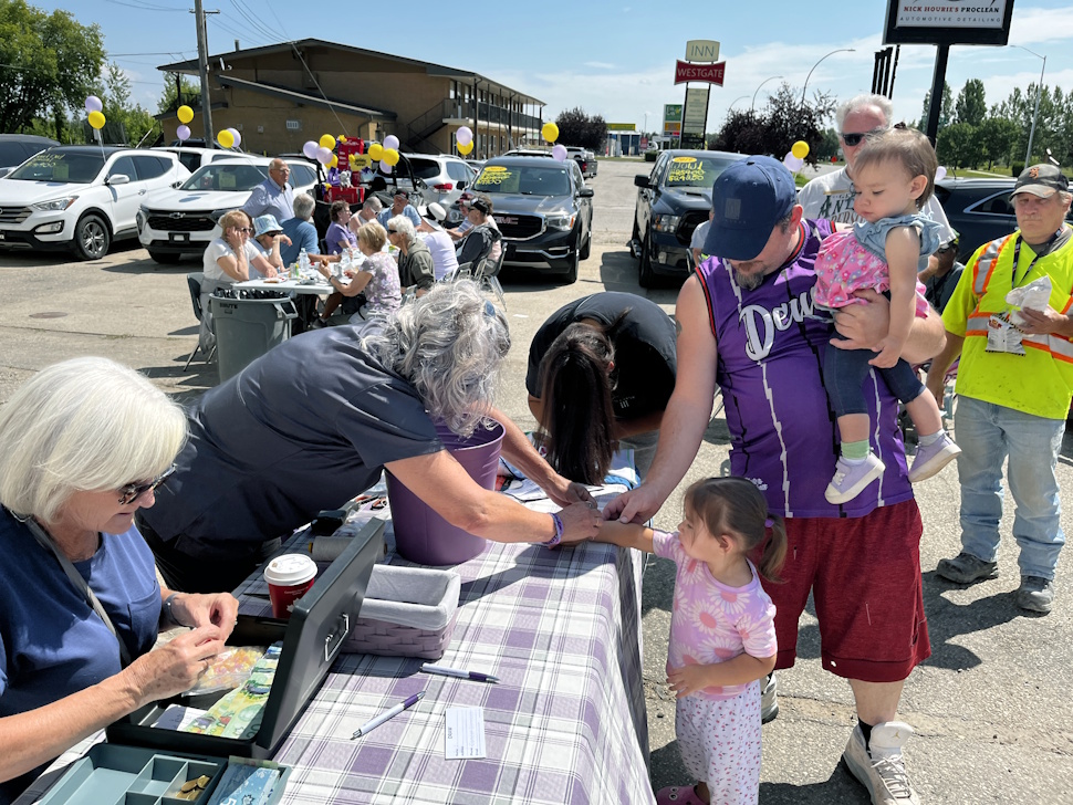Little girl smiling as she receives a UV-awareness bracelet at a fundraising barbecue event.