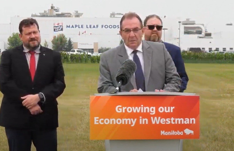 Agriculture Minister Ron Kostyshyn  standing outside Maple Leaf Foods plant at Brandon talking into a microphone at a podium as he makes the announcement