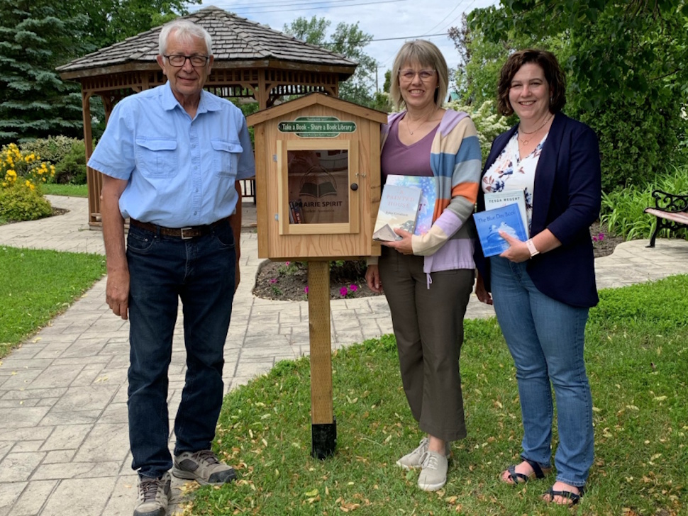 Gilles Guertin, Reeve of Norfolk-Treherne, Alison Delf-Timmerman, PSTA Public Relations Co-Chair, and Patti Everett, PSTA public relations volunteer, stand together by the little library at Central Park in Treherne.