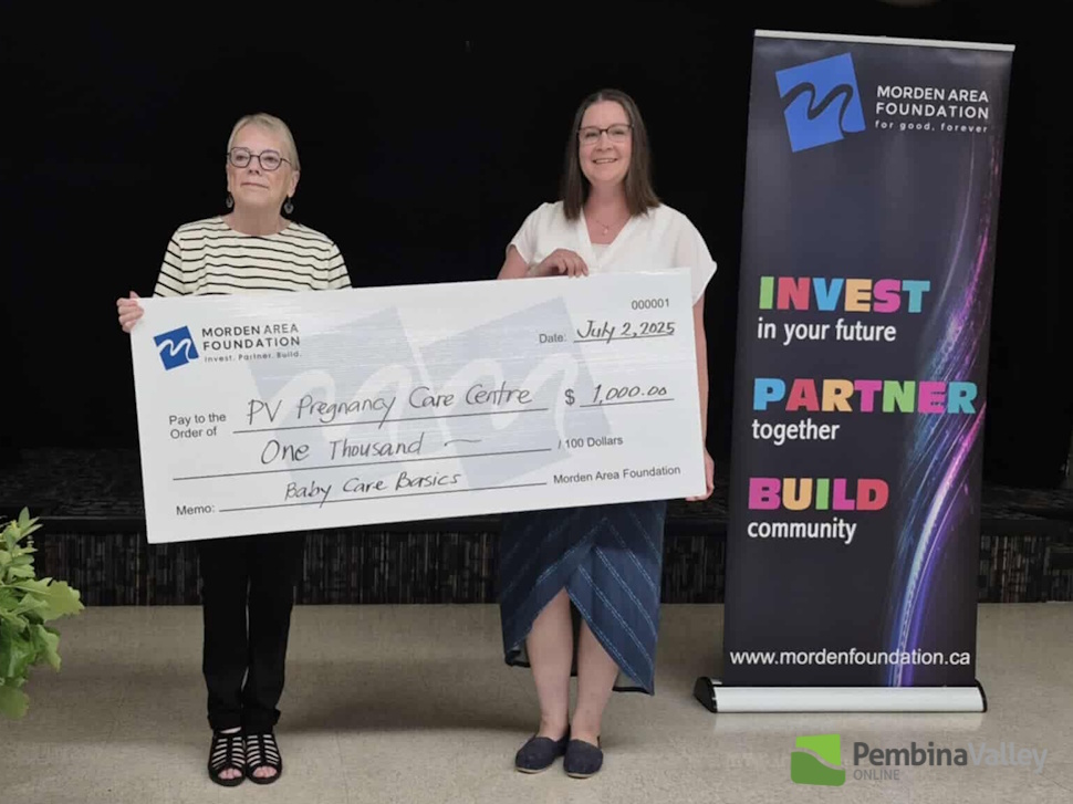 two women stand behind a giant cheque