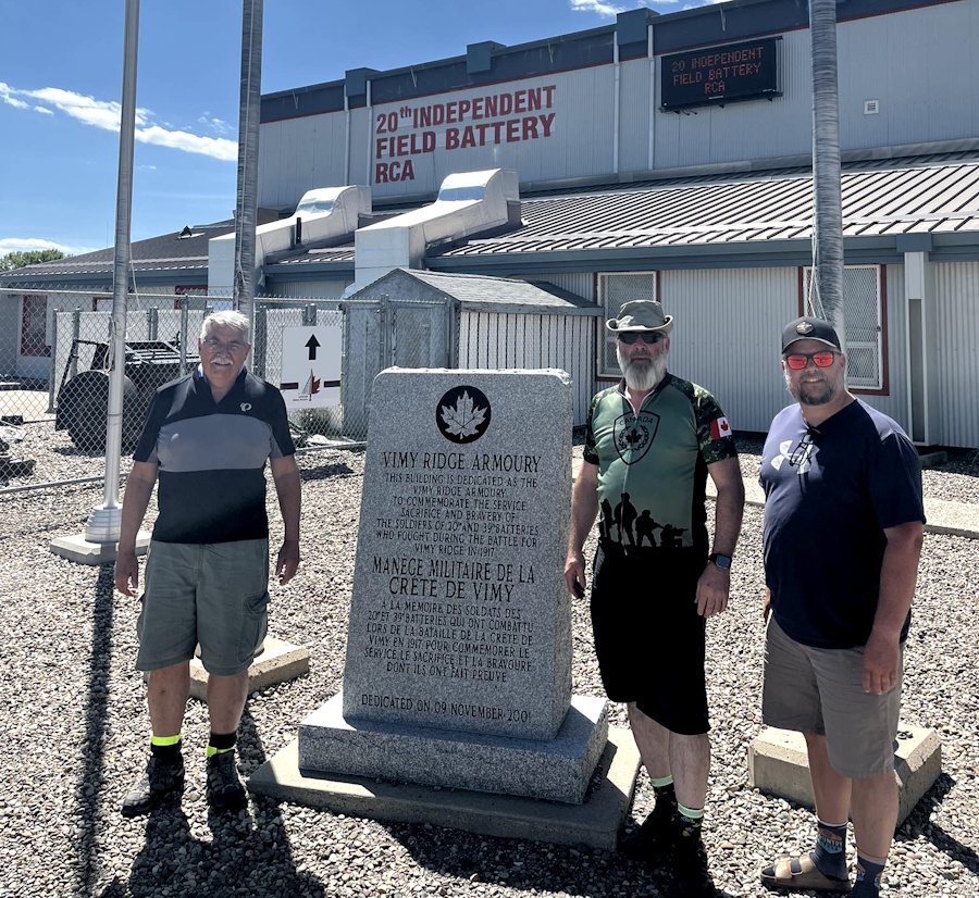 Three men stand at a monument at an armoury
