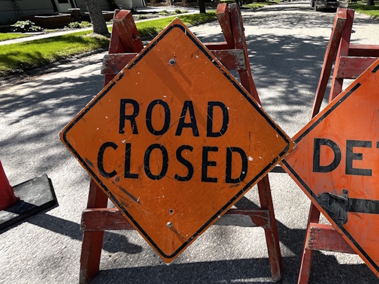 Orange road closed sign placed in front of a blocked residential street during a water service repair.