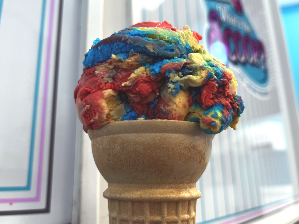 A colorful ice cream cone topped with swirls of vibrant pink, blue, yellow, and green ice cream — the popular “Superhero” flavour.