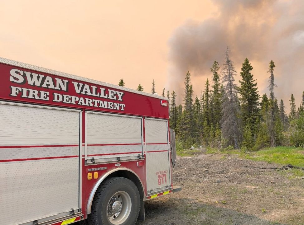 a fire truck from the Swan Valley Fire Department with a blazing forest fire behind it