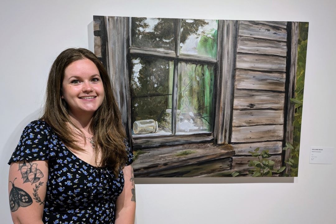 Artist Hollande Bezan posing with one of her paintings in 'Return to the Farm' at Gallery in the Park.