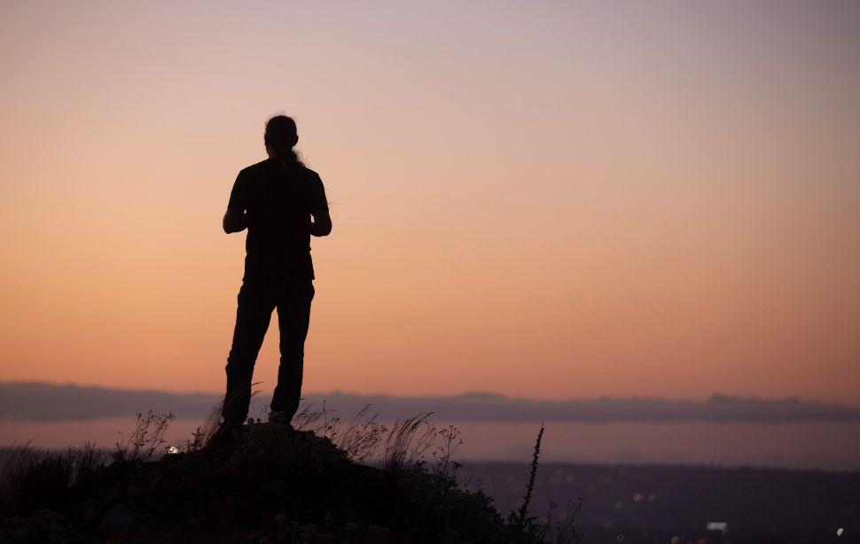 A silhouette of a person standing on a hill overlooking a smoky skyline