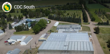 Large square building with greenhouses, quonsets and other buildings with trees