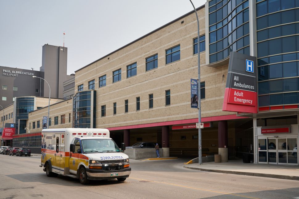 An ambulance drives down a street with the entrance to the HSC emergency seen in the background