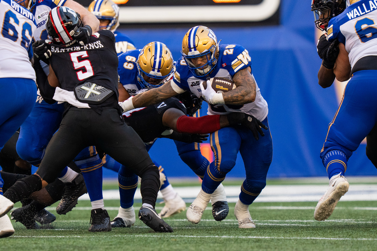 A Winnipeg Blue Bombers player runs with the ball tucked against their body as teammates block opposing players