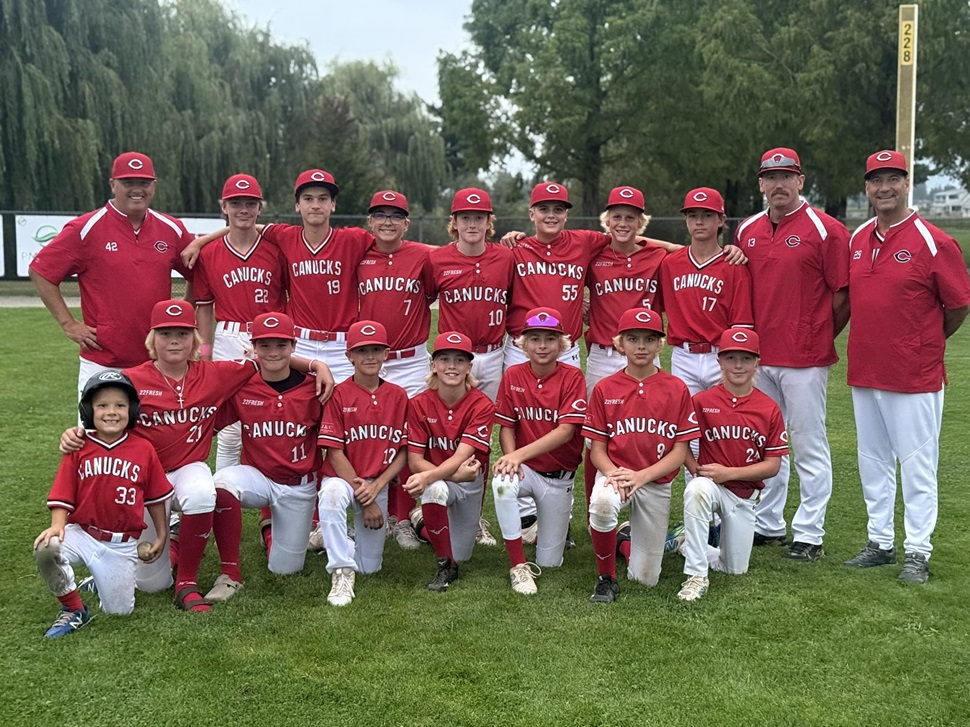  Group photo of the U13 AAA Canucks baseball team in red jerseys and white pants, with players kneeling in front and standing behind, flanked by three coaches in red shirts. Trees and a baseball field are visible in the background.