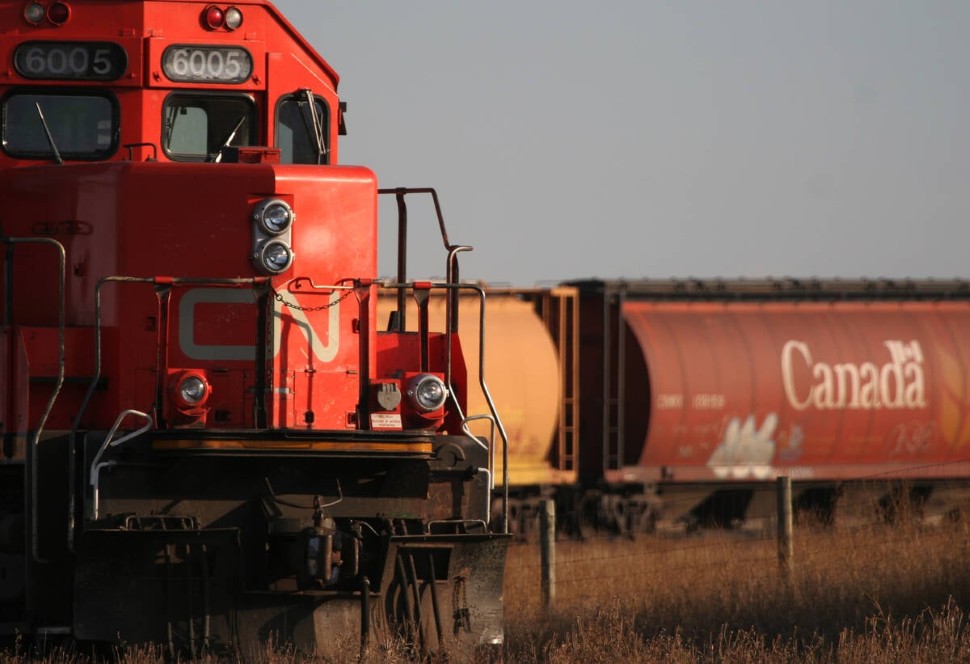  The nose of a CN train engine rounding a corner is in the foreground with its grain cars visible in the background.