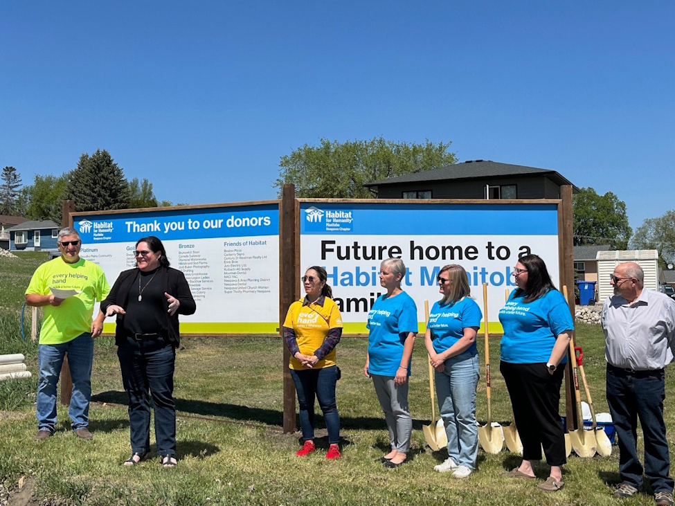 a woman speaks to a crowd at a Habitat for Humanity build site