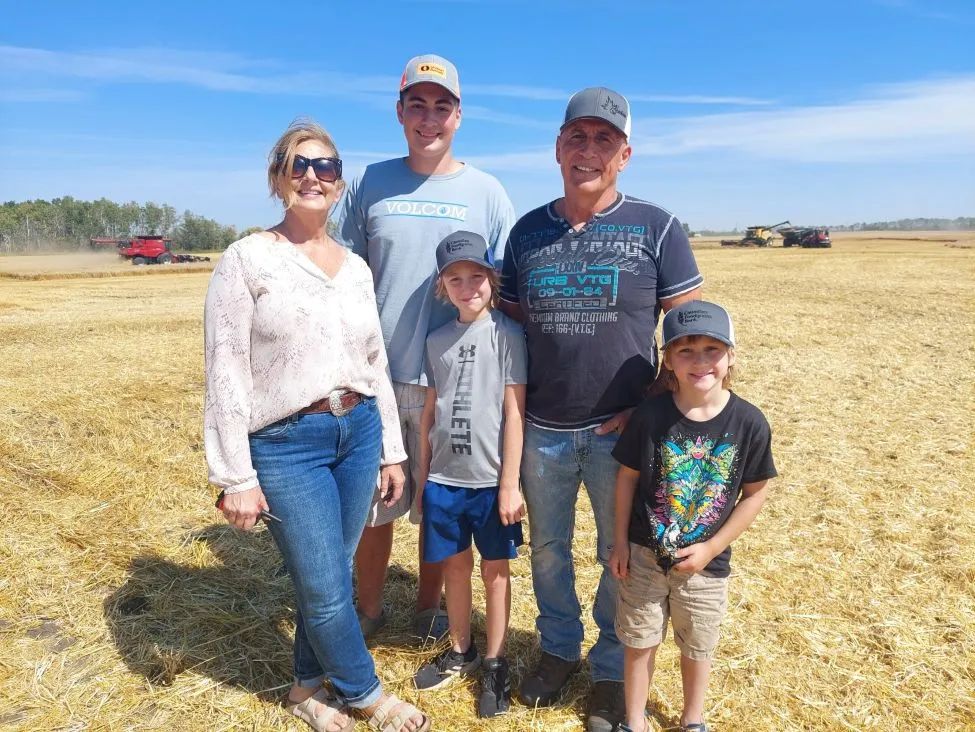 A family of 5, a husband, wife, and 3 boys, stand in a grain field