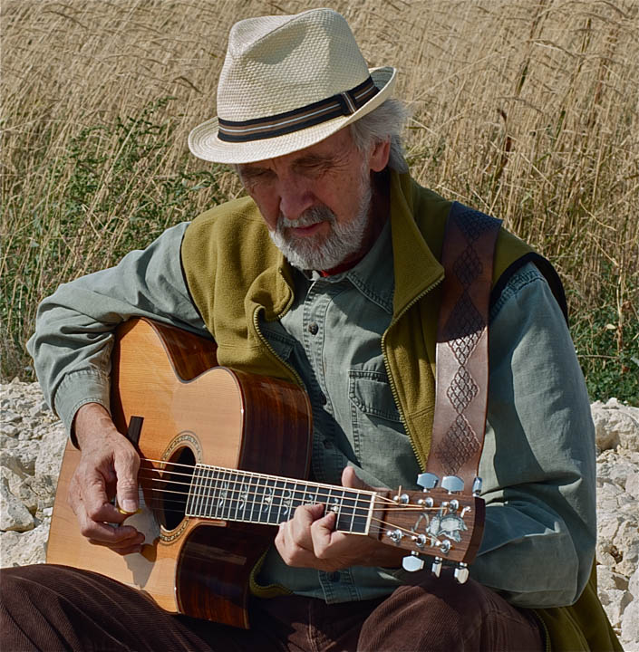 Entertainer Fred Penner is shown in this photo. He's wearing a nice hat and playing his guitar outdoors.