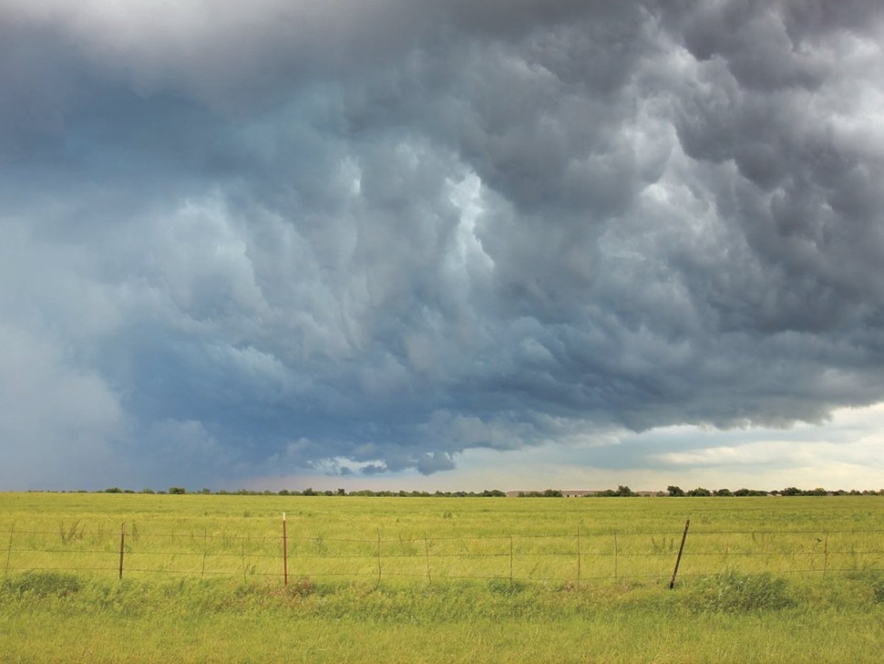   Dark storm clouds over a pasture with a page wire fence in the foreground.
