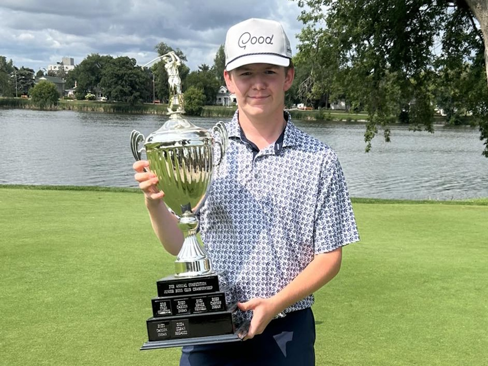 Logan Cairns smiling and holding the Portage Golf Club Junior Boys trophy outdoors on the golf course.