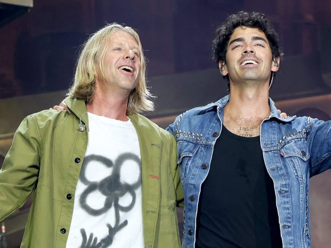 A man with blonde hair and a man with dark hair look out from a stage