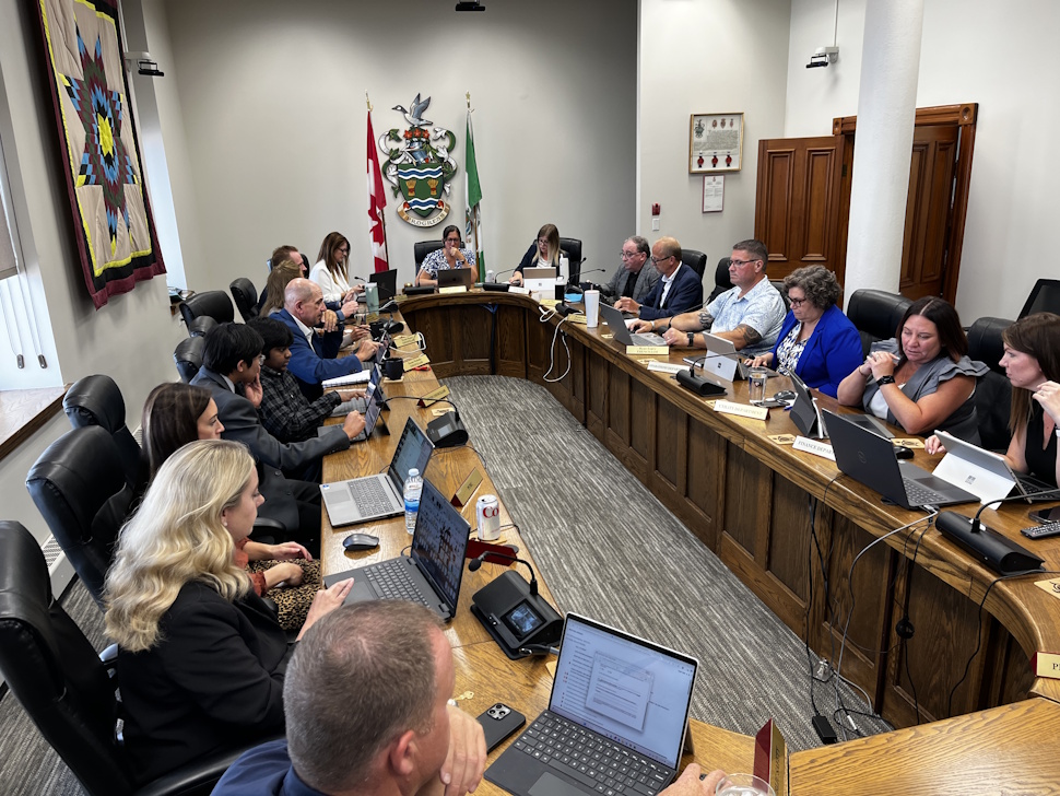 City council chambers at the August 11 meeting, showing councillors seated around the horseshoe-shaped table with microphones and documents.