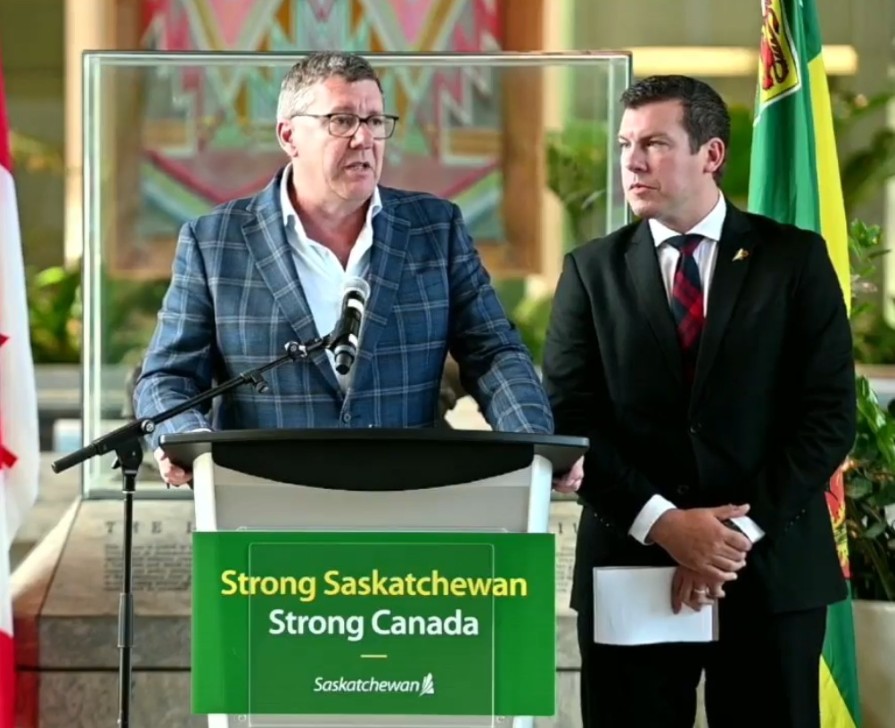 Premier Scott Moe standing at a mic with Liberal MP Kody Blois to his left
