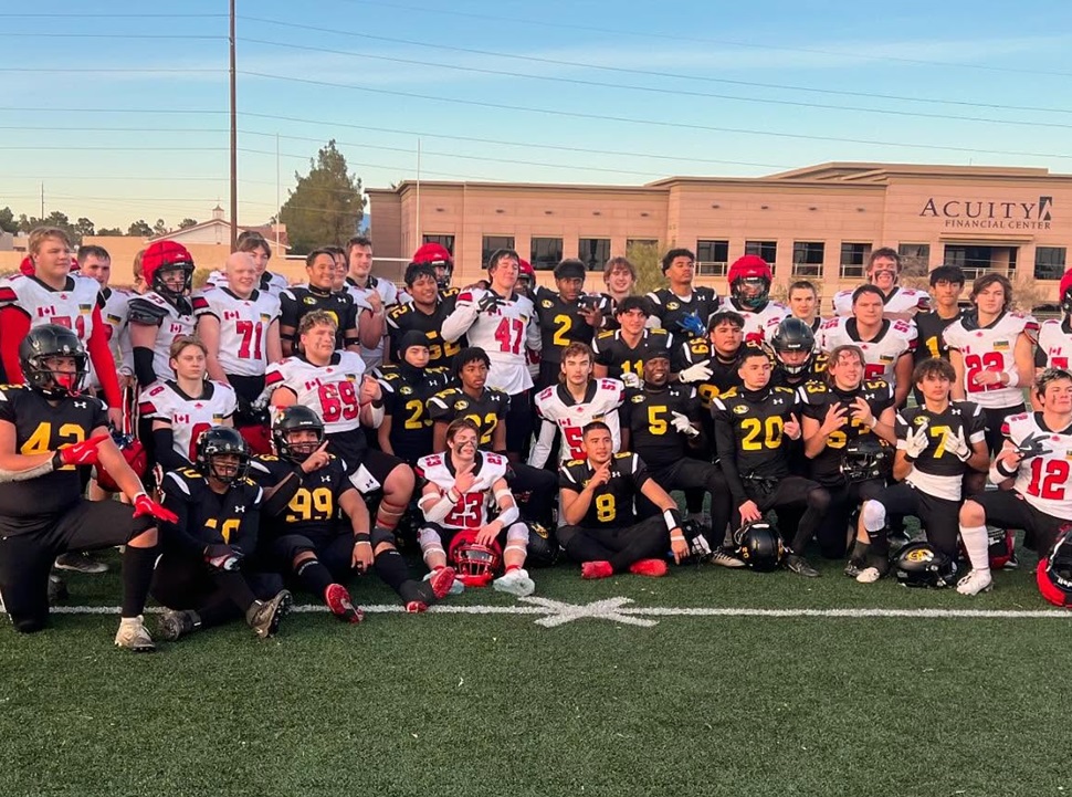 A group of football players pose on a field in front of a building labeled "ACUITY FINANCIAL CENTER." They wear two different uniforms—black with yellow numbers and white with red numbers.