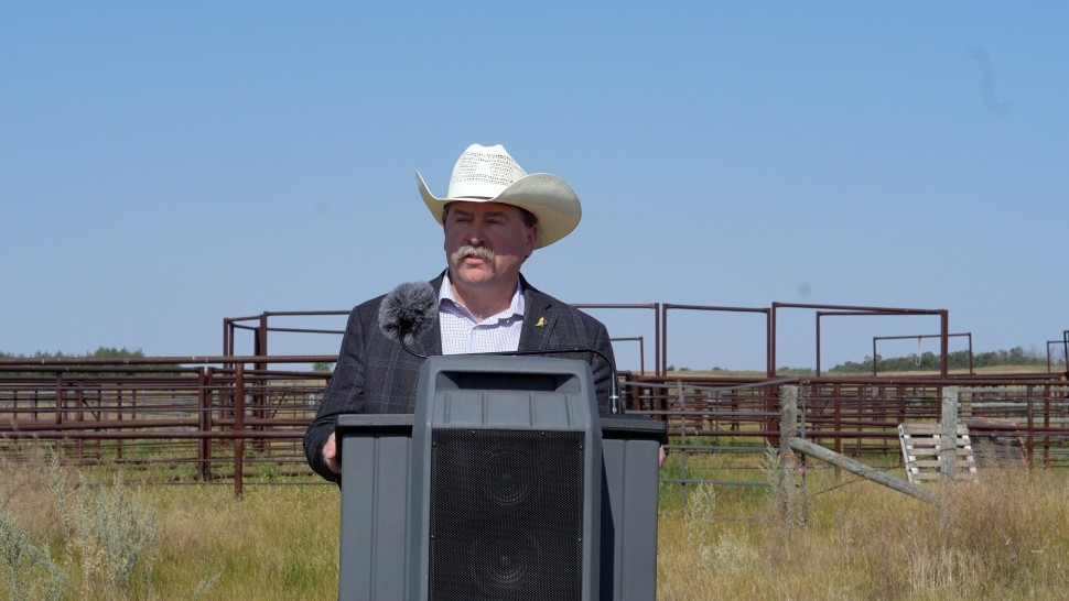 Agriculture Minister Daryl Harrison outside at a pasture standing at a microphone and podium in front of a corral 