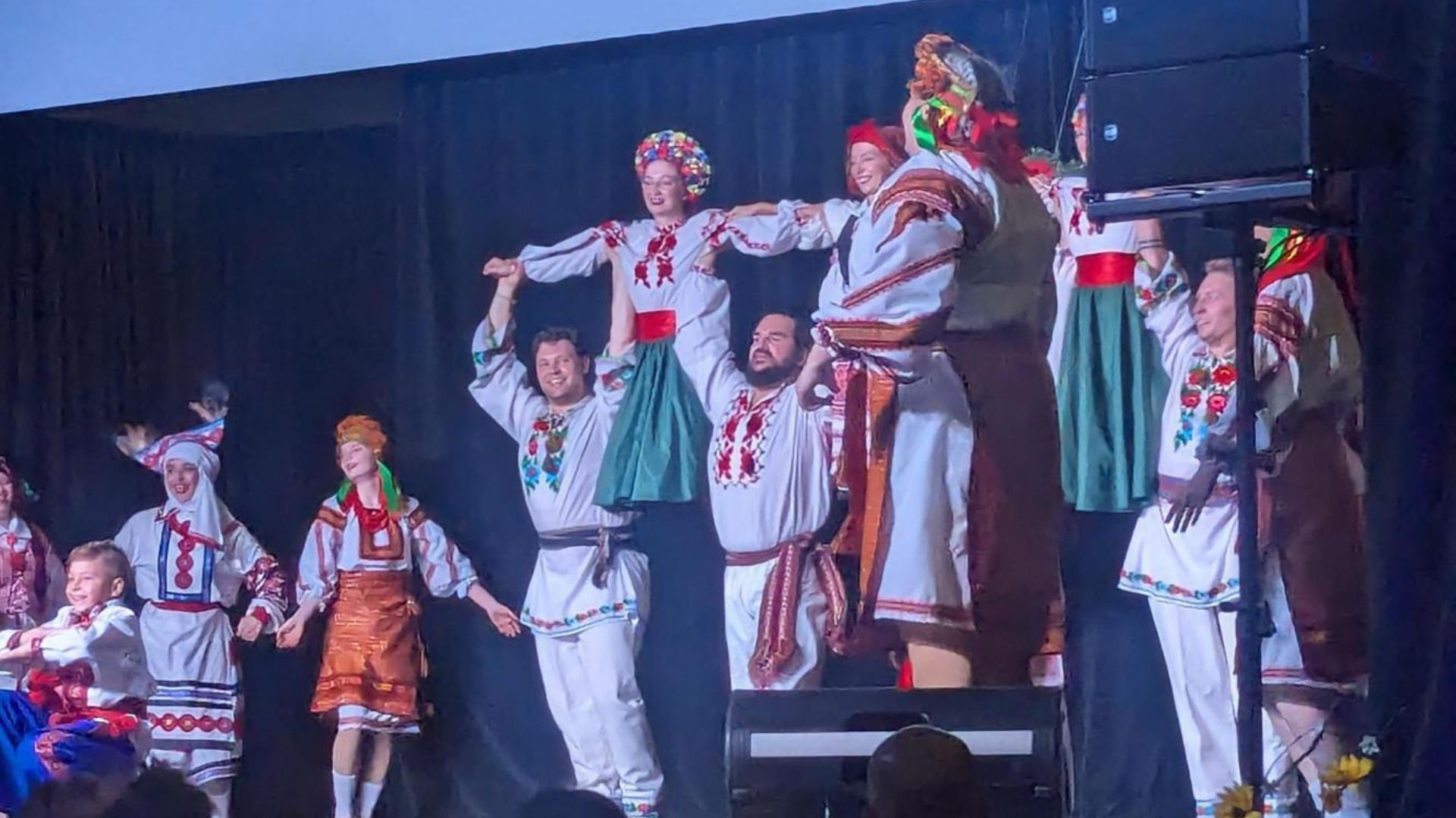 Ukrainian Dancers performing on stage in colourful costumes and people holding two dancers in the air