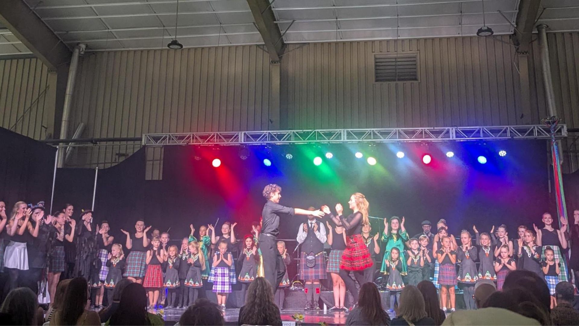 A large group of people on stage after putting on a show for the British Isles Pavilion in different costumes