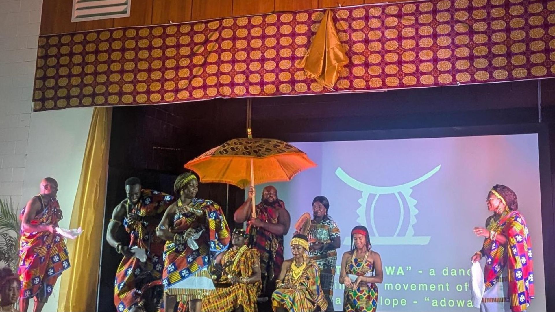 A reenactment of a Ghanaian royal procession on stage with people in traditional Ghanaian clothing and jewelry.