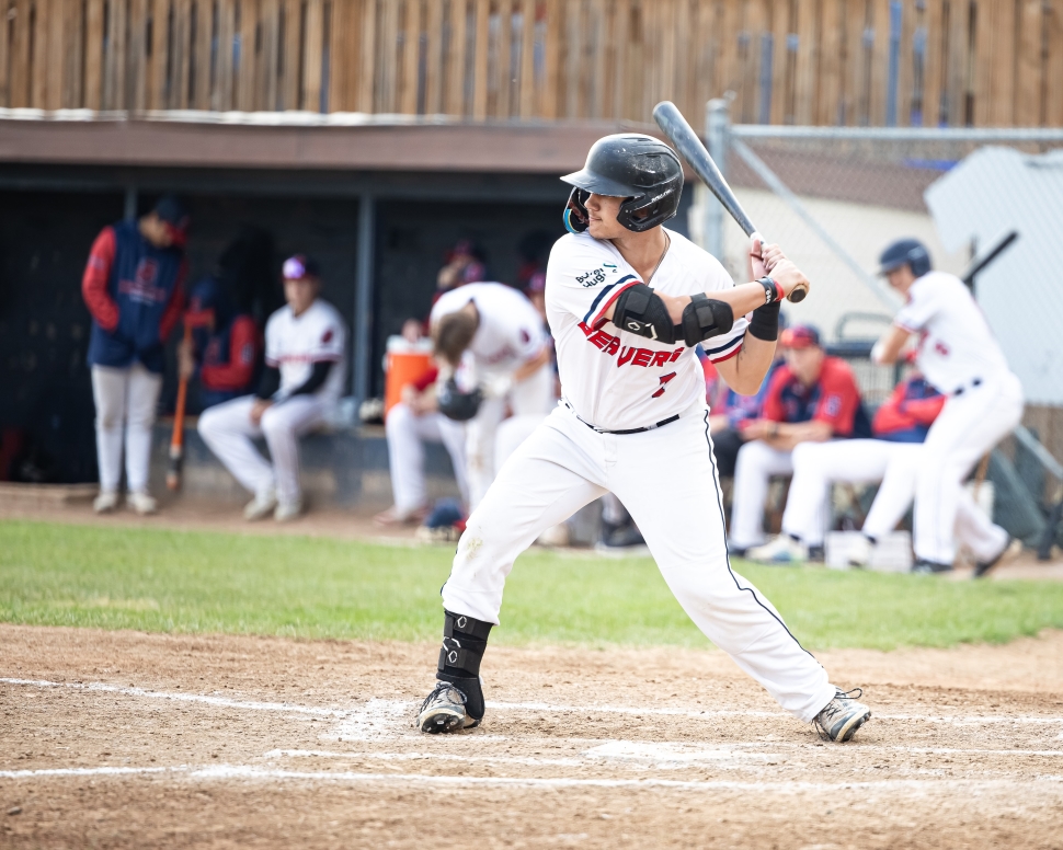 A baseball player in a white uniform swining his bat at the plate