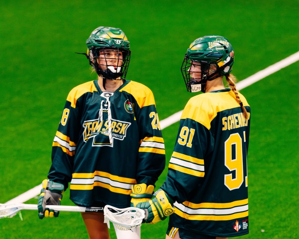 Two female lacrosse players in green uniforms standing and talking