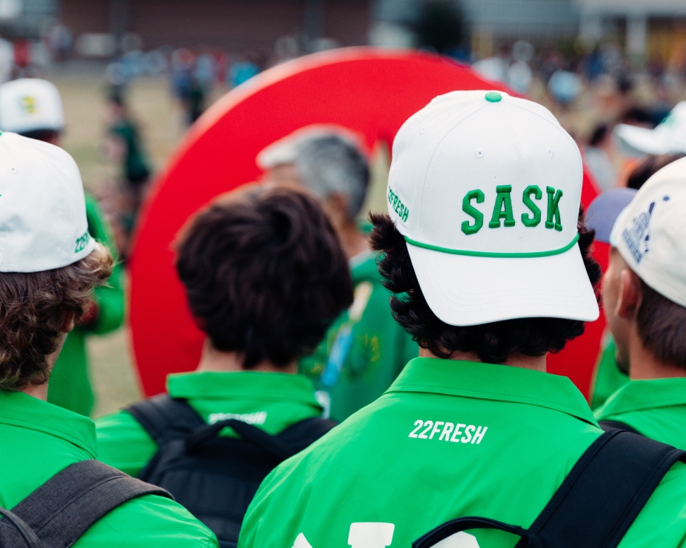 A person in a green jacket wearing a white cap that says SASK in green letters